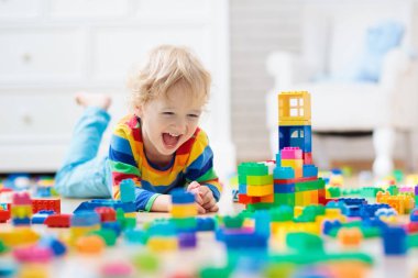 Çocuk renkli oyuncak bloklarıyla oynuyor. Küçük çocuk evde ya da kreşte kule inşa ediyor. Küçük çocuklar için eğitici oyuncaklar. Bebek ya da bebek için inşaat bloğu. Anaokulundaki oyun odasında karışıklık..