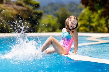 Çocuk havuzda oynuyor. Çocuklarla yaz tatili. Tropik bir adada egzotik tatilde suya atlayan küçük bir kız. Çocuklar yüzer. Anaokulu öncesi için aktif açık hava sporu.