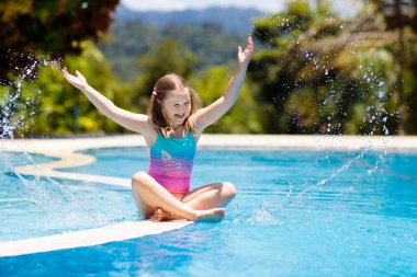 Çocuk havuzda oynuyor. Çocuklarla yaz tatili. Tropik bir adada egzotik tatilde suya atlayan küçük bir kız. Çocuklar yüzer. Anaokulu öncesi için aktif açık hava sporu.