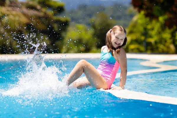 Çocuk havuzda oynuyor. Çocuklarla yaz tatili. Tropik bir adada egzotik tatilde suya atlayan küçük bir kız. Çocuklar yüzer. Anaokulu öncesi için aktif açık hava sporu.