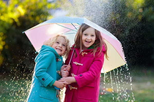 秋のシャワー雨の中で遊んでカラフルな傘を持つ子供たち 雨で公園で暖かいダッフルコート遊びの小さな男の子と女の子 子供のための屋外の楽しみを秋 雨を引く子供は — ストック写真