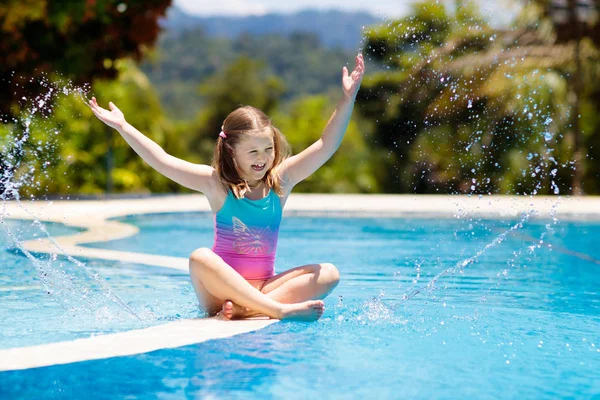 Çocuk havuzda oynuyor. Çocuklarla yaz tatili. Tropik bir adada egzotik tatilde suya atlayan küçük bir kız. Çocuklar yüzer. Anaokulu öncesi için aktif açık hava sporu.