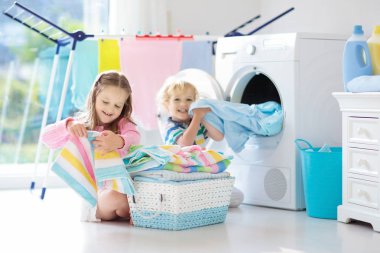 Çocuk Çamaşırhane, çamaşır makinesi ile Oda veya kurutma. Çocuklar aile işleri ile yardım. Modern ev aygıtları ve çamaşır deterjan beyaz güneşli evinde. Raf kurutma üzerinde temiz yıkanmış kıyafetler. 