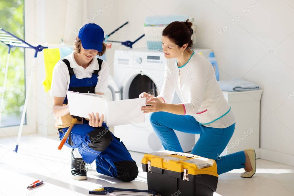 Washing machine repair service. Young technician examining and repairing tumble dryer. Woman looking at broken household appliance. Plumber with customer. Man fixing washer.
