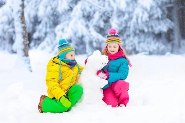在雪冬公园里做雪人的孩子们 孩子们在雪地里玩耍 男孩和女孩在五颜六色的夹克和帽子修造雪恐龙在冬天庭院在雪以后 冷冬日的户外娱乐 — 图库照片