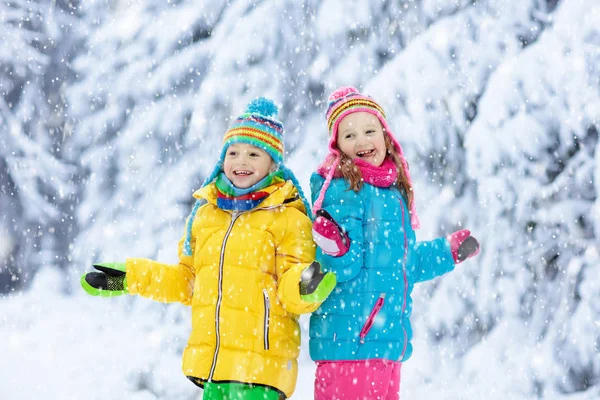 冬に雪で遊ぶ子供たち小さな女の子と男の子のカラフルなジャケットとニット帽子クリスマス冬の公園で雪をキャッチします 子供たちは 雪に覆われた森林にジャンプします 子供たちの雪合戦 — ストック写真