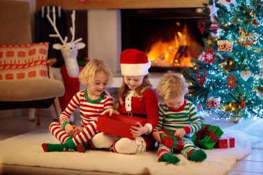 Noel arifesinde Noel ağacı ve şömine başında çocuklar. Noel 'i evde kutlayan çocuklu bir aile. Erkek ve kız aynı pijamaları giyip Noel ağacını süslüyor ve hediyeleri açıyor. Çocuklar için tatil hediyeleri.