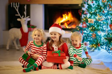 Noel arifesinde Noel ağacı ve şömine başında çocuklar. Noel 'i evde kutlayan çocuklu bir aile. Erkek ve kız aynı pijamaları giyip Noel ağacını süslüyor ve hediyeleri açıyor. Çocuklar için tatil hediyeleri.
