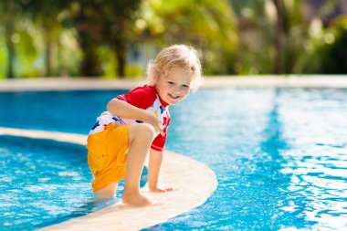 Çocuk havuzda oynuyor. Çocuklarla yaz tatili. Tropik bir adada egzotik tatilde suya atlayan küçük bir çocuk. Çocuklar yüzer. Anaokulu öncesi için aktif açık hava sporu.