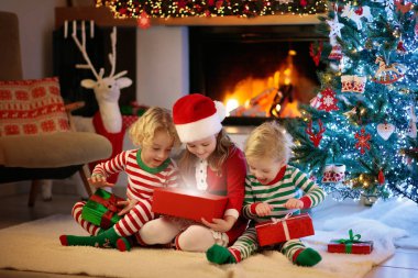 Noel arifesinde Noel ağacı ve şömine başında çocuklar. Noel 'i evde kutlayan çocuklu bir aile. Erkek ve kız aynı pijamaları giyip Noel ağacını süslüyor ve hediyeleri açıyor. Çocuklar için tatil hediyeleri.