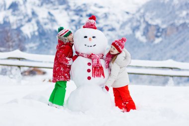 Kardan adam yapan çocuk. Çocuklar kardan adam yapar. Erkek ve kız, karlı kış gününde dışarıda oynuyorlar. Noel tatilinde dağlarda aile eğlencesi. Çocuklar İsviçre dağ manzarasında oynuyorlar..