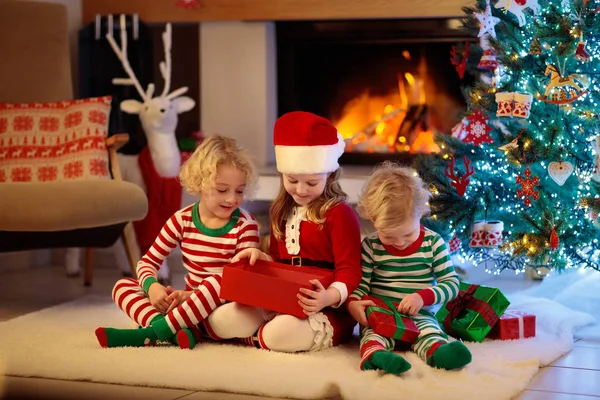 クリスマスツリーの子供たちとクリスマスの前夜の暖炉 自宅でクリスマスを祝う子供たちと家族 夏の木やオープニングプレゼントを飾るパジャマを着た男の子と女の子 子供のための休日の贈り物 — ストック写真