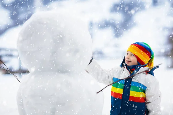 子供の建物の雪だるま 子供たちは 雪の男を構築します 雪の降る冬の日に野外で遊ぶ男の子 屋外クリスマス休暇に家族で楽しむ 小さな男の子再生雪のボールを飛行します 冬の衣類の活発な子供 — ストック写真