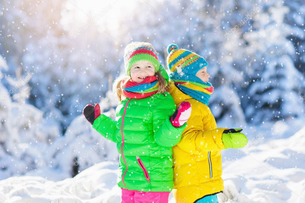 Children playing with snow in winter. Little girl and boy in colorful jacket and knitted hat catching snowflakes in winter park on Christmas. Kids jump in snowy forest. Snow ball fight for children.