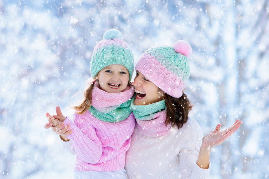 Mother and child in knitted winter hats play in snow on family Christmas vacation. Handmade wool hat and scarf for mom and kid. Knitting for kids. Knit outerwear. Woman and little girl in snowy park.