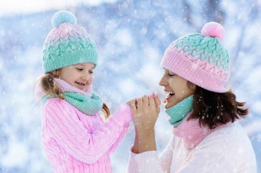 Kış şapkalı anne ve çocuk aile Noel tatilinde karda oynuyorlar. Anne ve çocuk için el yapımı yün şapka ve eşarp. Çocuklar için örgü örüyorum. Örgü dış giysi. Karlı parkta bir kadın ve küçük bir kız.