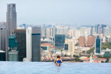 Çocuklar Singapur 'da aile tatilinde çatıda yüzüyorlar. Lüks oteldeki sonsuz havuzdan şehrin silüeti. Çocuklar Asya 'da yüzer ve gökdelen manzarasının tadını çıkarırlar. Küçük çocukla seyahat et..