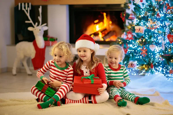 圣诞节前夕 孩子们在圣诞树和壁炉边 有孩子的家庭在家里庆祝圣诞节 男孩和女孩穿着搭配的睡衣装饰圣诞树和打开礼物 给孩子的节日礼物 — 图库照片