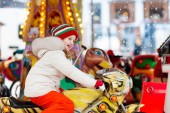 Kinder auf dem Weihnachtsmarkt. Kind beim traditionellen Straßenweihnachtsmarkt in Deutschland. Winter-Outdoor-Spaß. Kleines Mädchen mit Strickmütze reitet Karussell in Outdoor-Freizeitpark in der Winterferienzeit. 