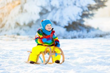 Küçük çocuk kızakla gezintiye çıkıyor. Çocuk kayağı. Kızak süren küçük bir çocuk. Çocuklar karda dışarıda oynarlar. Çocuklar kışın Alp dağlarında kızak kullanırdı. Aile Noel tatili için açık hava eğlencesi.
