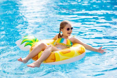 Şişme ananas yüzüklü çocuk yüzme havuzunda yüzüyor. Küçük kız yüzmeyi ve tropikal tatil köyü havuzuna dalmayı öğreniyor. Çocuklarla yüzmek. Çocuklar için sağlıklı bir spor. Su eğlencesi