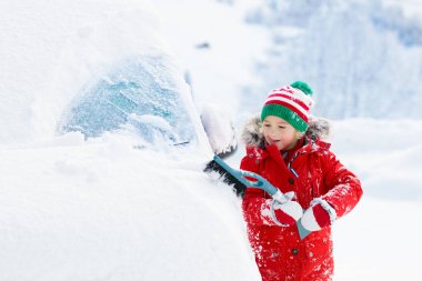 Çocuk fırtına üstüne kar temizliyor. Kış fırçası ve kazıyıcısı olan çocuk bir gecede kar fırtınasından sonra aile arabasını temizliyor. Dağlarda aile Noel tatili. Kar kürüyen çocuklar.