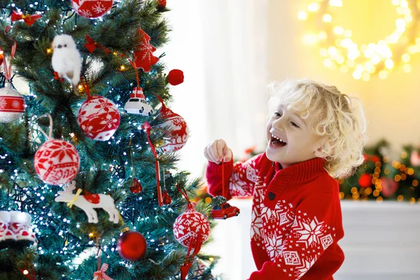 子供は自宅のクリスマス ツリーを飾るします クリスマス飾り付きニット セーターの少年 子供を持つ家族は 冬の休日を祝うため 子供たちはクリスマスのためのリビング ルームと暖炉を飾る — ストック写真