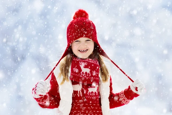 クリスマス休暇に雪の中で遊ぶ赤い帽子の子供 冬の屋外の楽しみ Xmas Eveの雪の公園で子供たちが遊ぶ ニットセーター スカーフの女の子とクリスマスの装飾でミトン — ストック写真