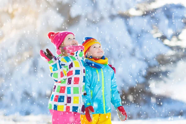 Kids playing in snow. Children play outdoors on snowy winter day. Boy and girl catching snowflakes in snowfall storm. Brother and sister throwing snow balls. Family Christmas vacation activity.