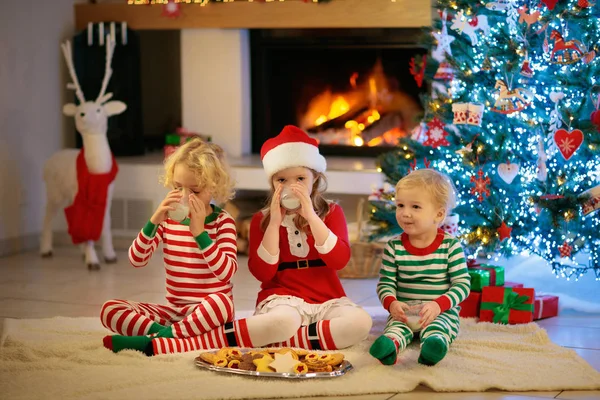クリスマス ツリーと暖炉で子供は ホット チョコレートを飲むし クリスマスイブにクッキーを食べる 家族子供の家庭でクリスマスを祝います 男の子と女の子のプレゼントを開けます 子供のクリスマス プレゼント — ストック写真