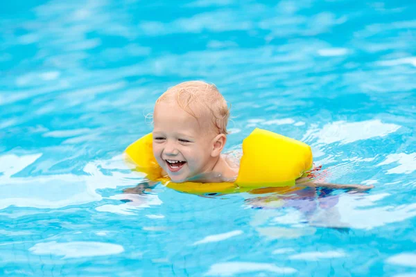 Baby with inflatable armbands in swimming pool. Little boy learning to swim in outdoor pool of tropical resort. Swimming with kids. Healthy sport activity for children. Summer vacation. Swim aids.