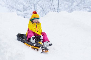 Küçük kız kızakla gezintiye çıkıyor. Çocuk kayağı. Kızak süren küçük bir çocuk. Çocuklar karda dışarıda oynarlar. Çocuklar kışın Alp dağlarında kızak kullanırdı. Aile Noel tatili için açık hava eğlencesi.