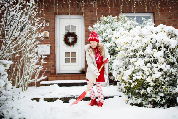 子供のシャベル雪 冬の吹雪の後に舗装されたクリアドライブウェイを持つ少女 クリスマスの吹雪の後 子供たちは家のドアへの明確なパス 雪の楽しみ 寒い霜の庭で遊ぶ子供たち — ストック写真