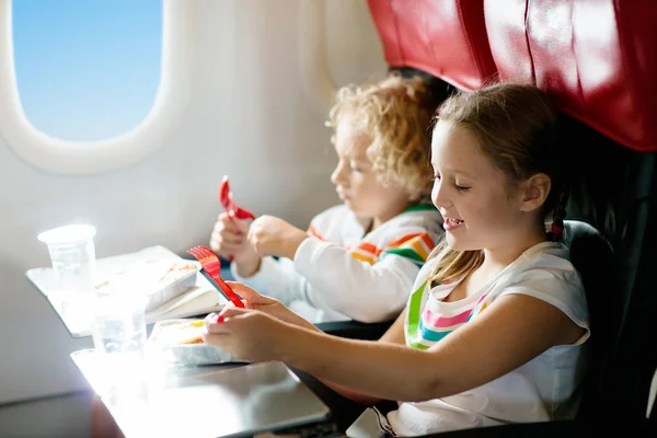 Child in airplane window seat. Kids flight meal. Children fly. Special inflight menu, food and drink for baby and kid. Girl and boy eating healthy lunch in airplane. Travel and family vacation.