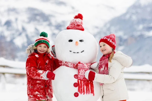 子供が雪だるまを作る 子供は雪男を作る 冬の雪の日に屋外で遊ぶ男の子と女の子 山の中でクリスマス休暇に屋外の家族の楽しみ 子供たちはスイスの山の風景で遊ぶ — ストック写真