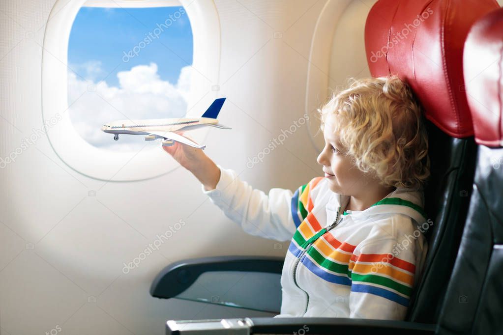 Child in airplane. Kid in air plane sitting in window seat. Flight entertainment for kids. Traveling with young children. Kids fly and travel. Family summer vacation. Little boy with toy in airplane.