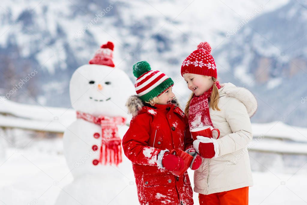 Child building snowman. Kids build snow man. Boy and girl playing outdoors on snowy winter day. Outdoor family fun on Christmas vacation in the mountains. Children play in Swiss mountain landscape.