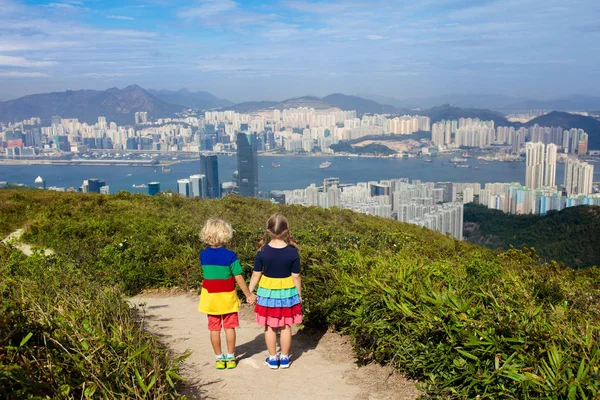 Family with kids hiking in Hong Kong mountains. Beautiful landscape with hills, sea and city skyscrapers in Hong Kong, China. Outdoor activity in the nature for parents and children.