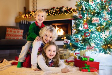 Noel arifesinde Noel ağacı ve şömine başında çocuklar. Noel 'i evde kutlayan çocuklu bir aile. Erkek ve kız aynı pijamaları giyip Noel ağacını süslüyor ve hediyeleri açıyor. Çocuklar için tatil hediyeleri.