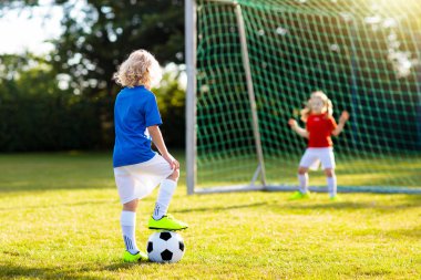 Çocuklar dışarıda futbol oynarlar. Çocuklar futbol maçında gol atıyor. Küçük çocuk topa vuruyor. Formalı ve kramponlu koşan çocuk. Okul futbol kulübü. Genç oyuncu için spor eğitimi.