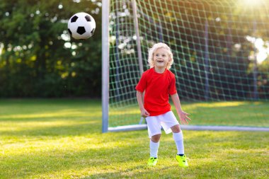 Çocuklar dışarıda futbol oynarlar. Çocuklar futbol maçında gol atıyor. Küçük çocuk topa vuruyor. Formalı ve kramponlu koşan çocuk. Okul futbol kulübü. Genç oyuncu için spor eğitimi.