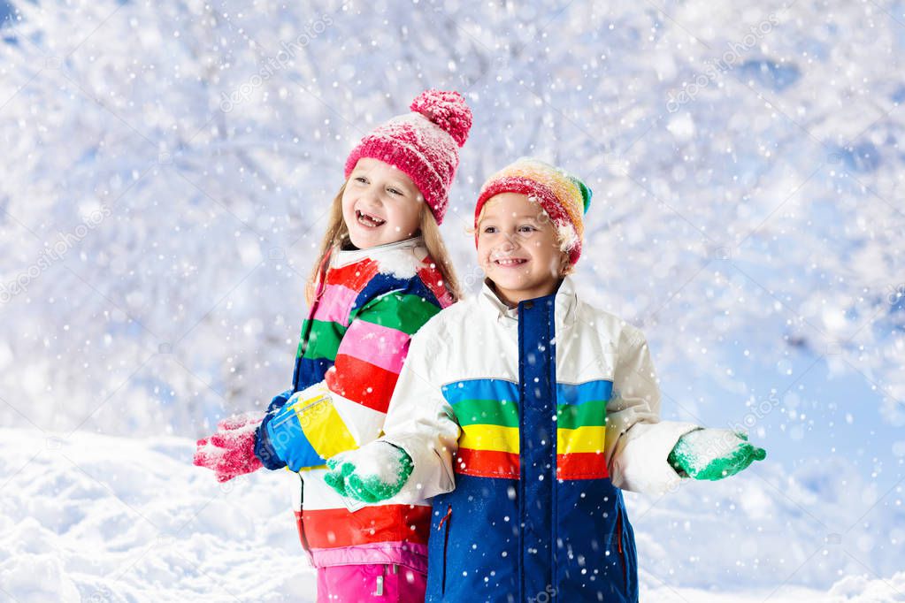 Kids playing in snow. Children play outdoors on snowy winter day. Boy and girl catching snowflakes in snowfall storm. Brother and sister throwing snow balls. Family Christmas vacation activity.