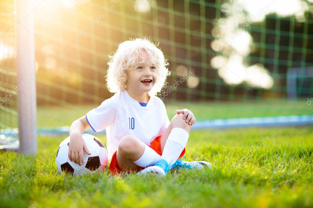 Kids play football on outdoor field. England team fans. Children score a goal at soccer game. Little boy in English jersey and cleats kicking ball. Football pitch. Sports training for player.