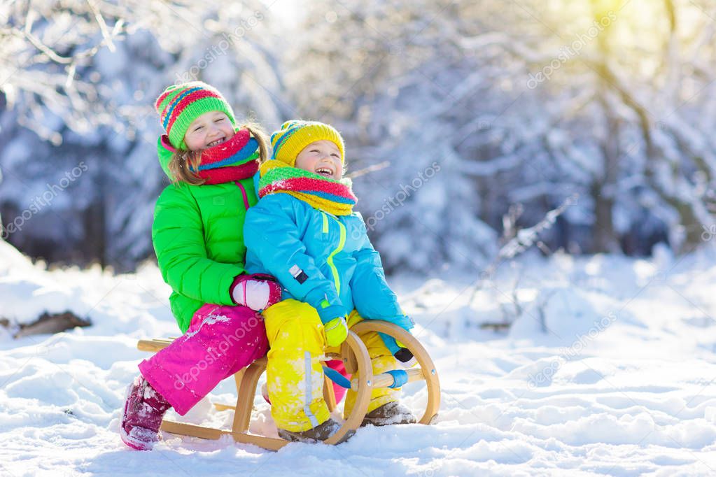 Little girl and boy enjoying sleigh ride. Child sledding. Toddler kid riding a sledge. Children play outdoors in snow. Kids sled in snowy park in winter. Outdoor fun for family Christmas vacation.