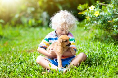 Kids sevimli küçük köpek yavrusu ile oynamak. Çocuk ve bebek köpekler güneşli yaz bahçede oynarken. Küçük kız holding yavru. Çocuk ile evde beslenen hayvan köpek. Aile ve park'ın bahçesinde evcil hayvan. Çocuk ve hayvan dostluk.