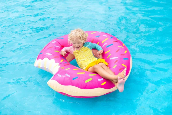 Child in swimming pool on funny inflatable donut float ring. Little boy learning to swim in outdoor pool of tropical resort. Water toys for kids. Healthy sport activity for children. Sun protection.