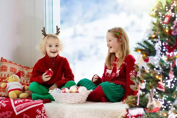孩子们在家里装饰圣诞树 穿着针织毛衣 手持圣诞装饰品的小男孩和小女孩 家里人庆祝寒假 孩子们在圣诞节装饰客厅和窗户 — 图库照片