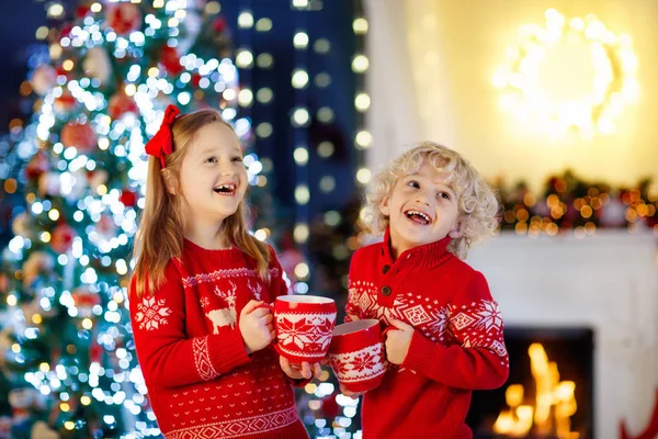 孩子在圣诞树下在家 小男孩和女孩在针织毛衣与圣诞节装饰品喝热巧克力 家庭与孩子庆祝寒假 孩子们在壁炉边打开礼物 — 图库照片