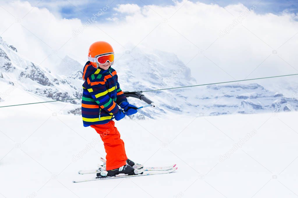 Child on a button ski lift going uphill in the mountains on a sunny snowy day. Kids in winter sport school in alpine resort. Family fun in the snow. Little skier learning and exercising on a slope.