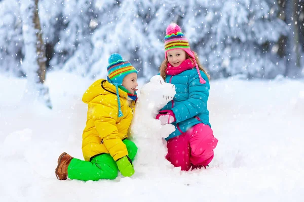 在雪冬公园里做雪人的孩子们 孩子们在雪地里玩耍 男孩和女孩在五颜六色的夹克和帽子修造雪恐龙在冬天庭院在雪以后 冷冬日的户外娱乐 — 图库照片